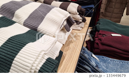 Folded striped and solid knit sweaters displayed on a wooden table in a cozy clothing store 133449679