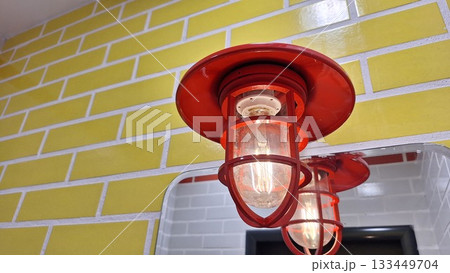 Red industrial light fixture against yellow brick wall in modern interior Red industrial light fixture against yellow brick wall in modern interior 133449704