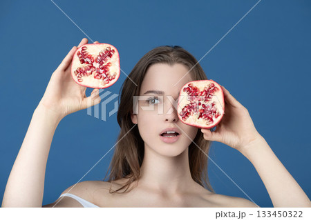 Beautiful young woman covering her eye with pomegranate fruit slices Beautiful young woman covering her eye with pomegranate fruit slices 133450322