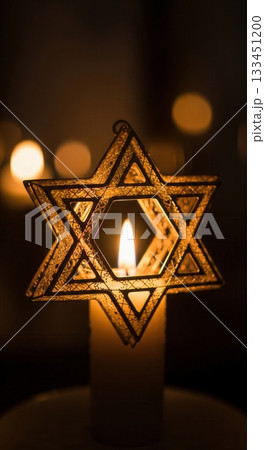 A close-up of a Star of David ornament illuminated by a single candle flame. The warm, glowing light creates a spiritual and peaceful mood. Ideal for Hanukkah or memorial concepts. 133451200