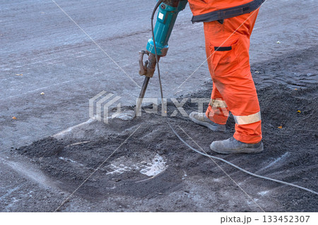 Repair.A road worker breaks up old asphalt with a jackhammer 133452307