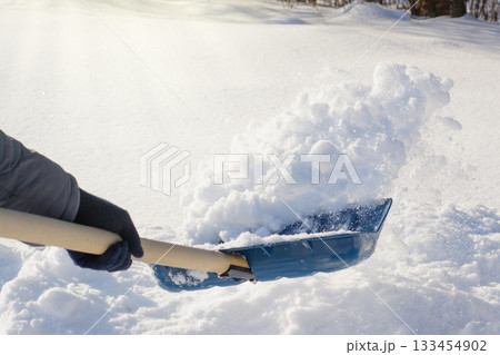 City service cleaner with blue shovel while cleaning sidewalks in the park after a heavy snow 133454902