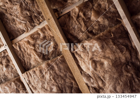 Fiberglass is used as warming material on a ceiling in a private house. Glass wool in a wooden frame on a wall. 133454947