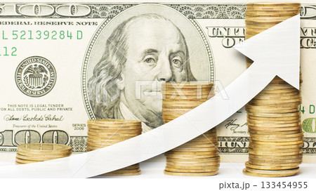 Close up photo of golden coins with white arrow showing upward direction against a one hundred US dollar bill at the background Close up photo of golden coins with white arrow showing upward direction against a one hundred US dollar bill at the background 133454955