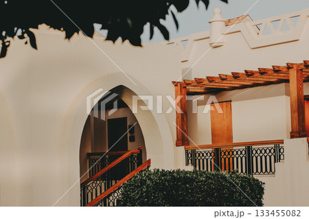 Elegant architectural detail of a Mediterranean-style building Captured at golden hour, image showcases facade featuring arches, wooden pergolas, ornamental wrought iron railings. Inviting aesthetic. Elegant architectural detail of a Mediterranean-style building Captured at golden hour, image showcases facade featuring arches, wooden pergolas, ornamental wrought iron railings. Inviting aesthetic. 133455082