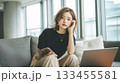 リビングでスマートフォンを手に悩む女性 133455581