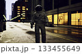 An astronaut stands solitary in a deserted city street illuminated by dim streetlights. Surrounding buildings reflect soft lights under the night sky. 133455649