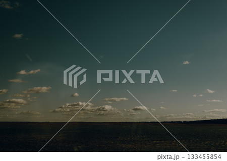 Dramatic sky over a cultivated field on a sunny day with scattered clouds. This image captures a serene landscape with a vast field under a beautiful sky, evoking a sense of peace and tranquility. 133455854