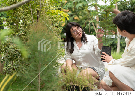 Two LGBTQ friends, one with long hair and the other with short hair, plant a tree in the morning garden. They share a joyful moment while caring for nature and nurturing new life in their home garden. Two LGBTQ friends, one with long hair and the other with short hair, plant a tree in the morning garden. They share a joyful moment while caring for nature and nurturing new life in their home garden. 133457412