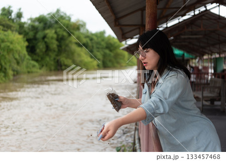 Two LGBTQ close friends feeding fish in the river at a Thai temple alms zone. The scene reflects kindness, spiritual practice, and their peaceful connection with nature. 133457468