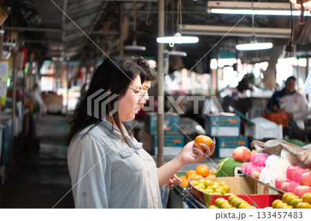 Two LGBTQ friends shopping for fresh fruits at a local Thai market. One holds an orange while the other selects vegetables. The atmosphere is vibrant and filled with colorful produce in a market. Two LGBTQ friends shopping for fresh fruits at a local Thai market. One holds an orange while the other selects vegetables. The atmosphere is vibrant and filled with colorful produce in a market. 133457483