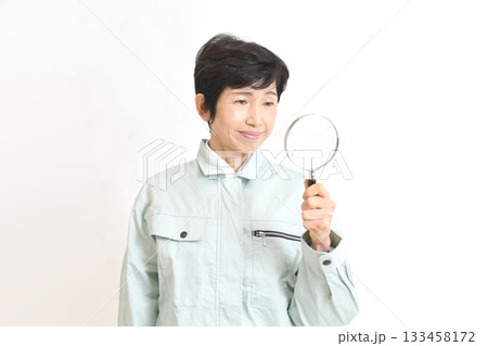 虫眼鏡を持つ作業服姿のアジア人のミドル女性 虫眼鏡を持つ作業服姿のアジア人のミドル女性 133458172