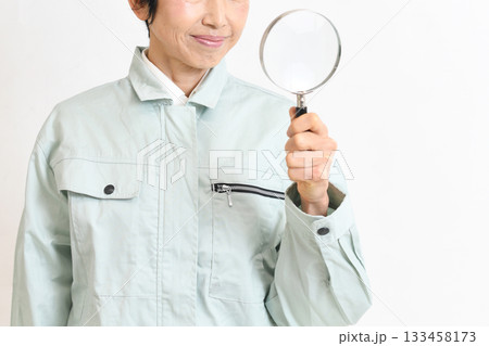 虫眼鏡を持つ作業服姿のアジア人のミドル女性 虫眼鏡を持つ作業服姿のアジア人のミドル女性 133458173