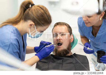 Two women dentists treating a man teeth Two women dentists treating a man teeth 133461844