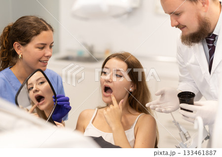 Male dentist helps a woman look at her repaired teeth in mirror Male dentist helps a woman look at her repaired teeth in mirror 133461887