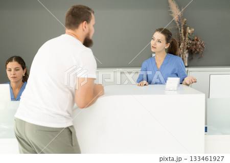 Dental clinic administrator talks to patients at reception desk Dental clinic administrator talks to patients at reception desk 133461927