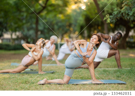 Women and men of different nationalities practicing yoga, doing revolved side angle pose in summer garden Women and men of different nationalities practicing yoga, doing revolved side angle pose in summer garden 133462031