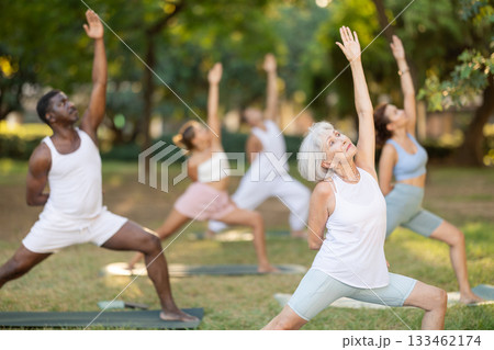 Senior woman performing Bound Reverse Warrior Pose at yoga class outdoors Senior woman performing Bound Reverse Warrior Pose at yoga class outdoors 133462174