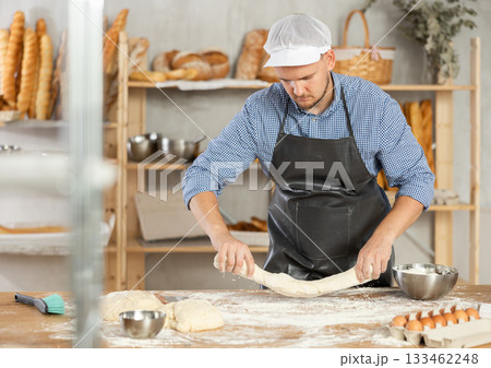Guy works as baker in bakery, molds sausages from dough, rolls long round strips from dough Guy works as baker in bakery, molds sausages from dough, rolls long round strips from dough 133462248