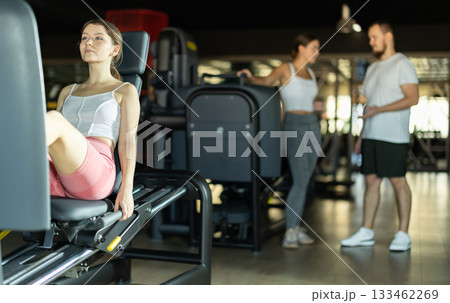 Slender athletic girl work out muscles of legs and thighs on simulator in fitness club Slender athletic girl work out muscles of legs and thighs on simulator in fitness club 133462269