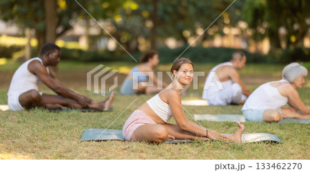 Multinational yoga enthusiasts with female coach perform Janu Shirshasana in park Multinational yoga enthusiasts with female coach perform Janu Shirshasana in park 133462270