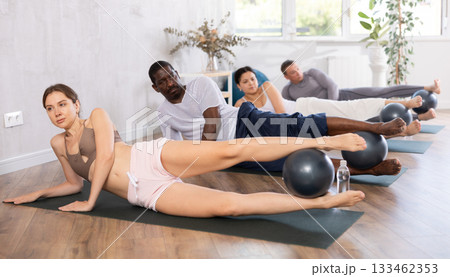 Group of active people doing soft ball pilates exercises during group pilates class in fitness gym Group of active people doing soft ball pilates exercises during group pilates class in fitness gym 133462353