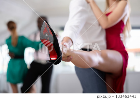 Elegant duet of a man and a woman in festive dresses dances a passionate tango during a group dance lesson in choreographic studio Elegant duet of a man and a woman in festive dresses dances a passionate tango during a group dance lesson in choreographic studio 133462443