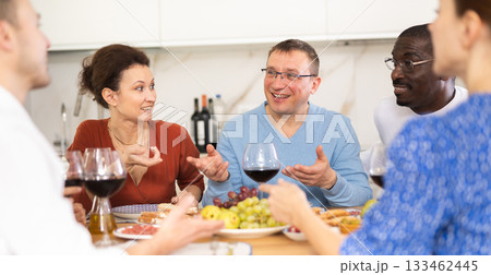 Companions congregated around a festive table, participating in animated discussions and enjoying the delights of red wine Companions congregated around a festive table, participating in animated discussions and enjoying the delights of red wine 133462445