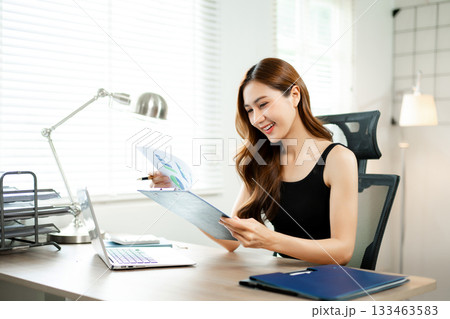 Confident Asian woman with a smile standing holding notepad and tablet at the modern office. 133463583