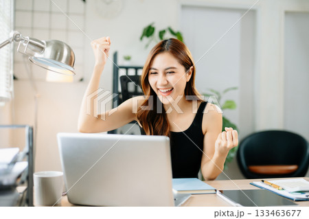 Cheerful businesswoman celebrating success at work, raising fists in joy at laptop, symbolizing achievement, motivation 133463677