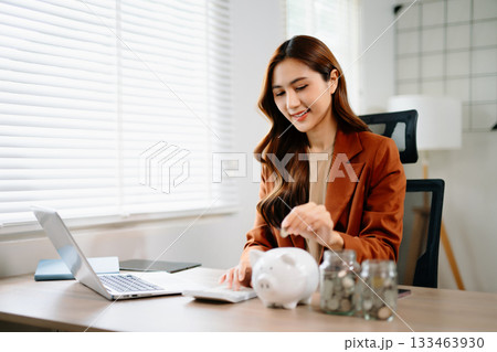 Smiling businesswoman saves money with piggy bank and coins. Ideal for finance, savings, budgeting, and office 133463930