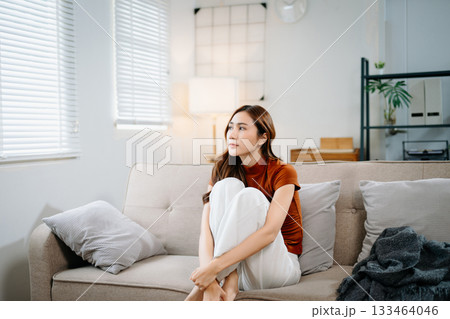 Sad Asian woman sitting on floor wrapped in blanket, holding head in distress. Concept of stress, anxiety, depression, burnout, and mental health problems. Sad Asian woman sitting on floor wrapped in blanket, holding head in distress. Concept of stress, anxiety, depression, burnout, and mental health problems. 133464046