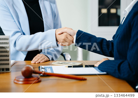 Business handshake in office with lawyer, cash, gavel, and building model. Concept of real estate deal, legal agreement, property contract, and investment success. 133464499