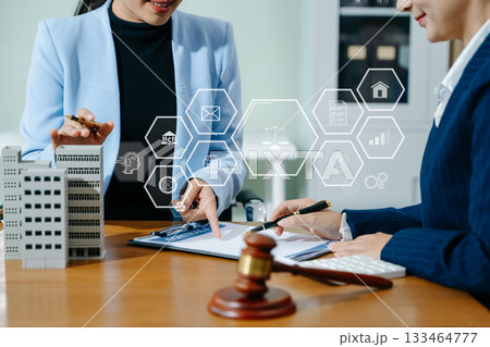 Female lawyer and client discuss legal contract with digital finance icons. Modern law, real estate, tech innovation, and business consulting in one powerful scene. 133464777