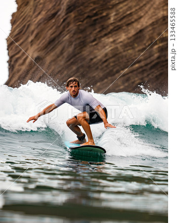 Surfer Expertly Rides a Wave Along a Rugged Coastline During Daylight Hours 133465588