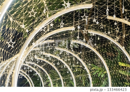 Curved white beams form an illuminated tunnel accented with hanging lights, and the structural lines create a clean pattern against the dark background. Curved white beams form an illuminated tunnel accented with hanging lights, and the structural lines create a clean pattern against the dark background. 133466423