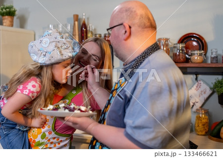 Family baking joy, Joyful family interaction during cake serving in warm kitchen setting, Celebrating family bonds with baking and sharing delicious strawberry cake 133466621