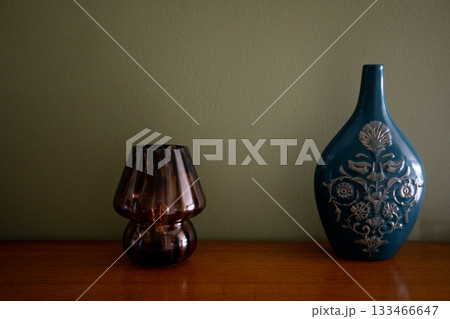 Stylish vintage setup with contrasting materials highlighting elegance, Decorative arrangement featuring colorful ceramics and translucent glassware with warm lighting 133466647