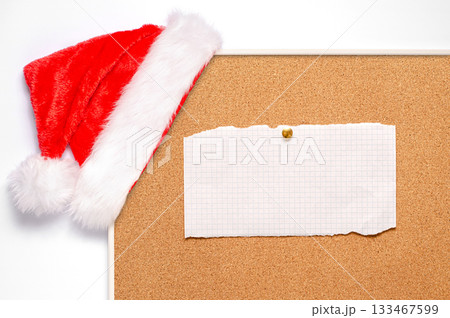 Blank note sheets are pinned to the board. Santa's hat on a cork board. Blank note sheets are pinned to the board. Santa's hat on a cork board. 133467599