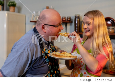 Joyful father and daughter meal, Laughter as family bonds over supper, Happy family sharing pizza in cozy kitchen surrounded by colorful decorations and retro appliances 133467708