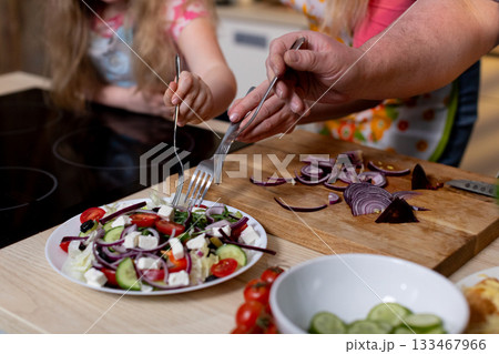 Colorful cooking scene, Young helper watches as ingredients are carefully assembled, Vivid kitchen atmosphere with child observing and participating in salad preparation 133467966