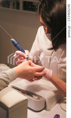 Manicure technique. Nail treatment. Female beautician hand in gloves removing cuticle with professional milling machine to create shape. 133468246