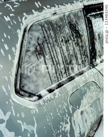 Bubbles and foam dance on a silver car during a bright afternoon wash at a local car cleaning spot 133469340