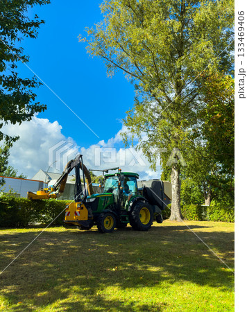 Tractor working under a bright blue sky while clearing land in a lush green field during a sunny afternoon Tractor working under a bright blue sky while clearing land in a lush green field during a sunny afternoon 133469406