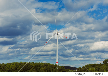Majestic wind turbine stands tall against a dramatic sky filled with fluffy clouds and vibrant greens of nature in a serene landscape at midday Majestic wind turbine stands tall against a dramatic sky filled with fluffy clouds and vibrant greens of nature in a serene landscape at midday 133469519