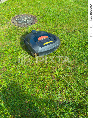 Robot mower navigating a green lawn under bright sunlight during a serene afternoon in a suburban neighborhood 133469592