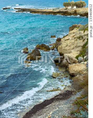 Waves crash against rugged cliffs while gentle breezes carry whispers of the ocean at a serene coastal lookout during a bright sunny day Waves crash against rugged cliffs while gentle breezes carry whispers of the ocean at a serene coastal lookout during a bright sunny day 133469612