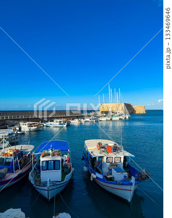 Colorful boats moored in a serene harbor under a bright blue sky near a historic fortress at midday 133469646