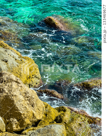 Bright turquoise waves crash gently against rocky shores, revealing the beauty of nature under the sun at midday along a serene coastal landscape Bright turquoise waves crash gently against rocky shores, revealing the beauty of nature under the sun at midday along a serene coastal landscape 133469677