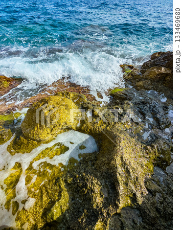 Waves crashing upon sunlit rocks by the shore in a beautiful coastal setting during the golden hour Waves crashing upon sunlit rocks by the shore in a beautiful coastal setting during the golden hour 133469680